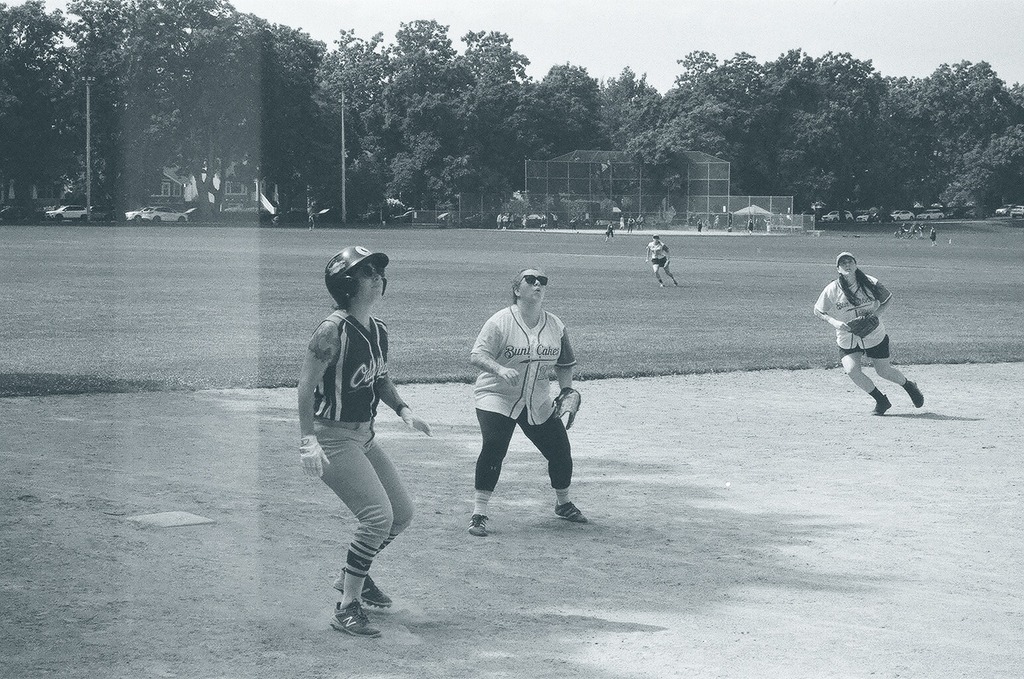 Shot of teammates on the field with one running and one waiting, and a player from an opposing team looking upwards.